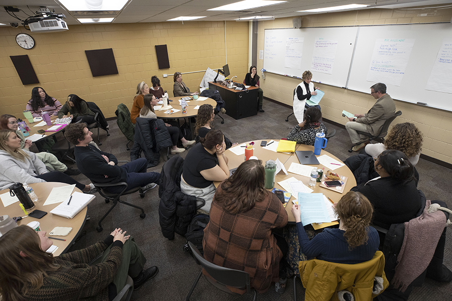 People sit in blue chairs around a large table with a large monitor.
