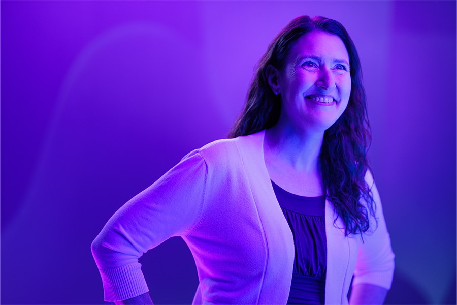 A person smiles off to the side with purple lighting.